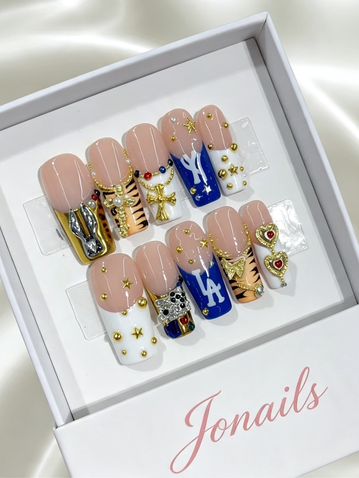 Y2K mixed style press-on nails with nude base, tiger stripes, blue NY LA lettering and 3D gold charms